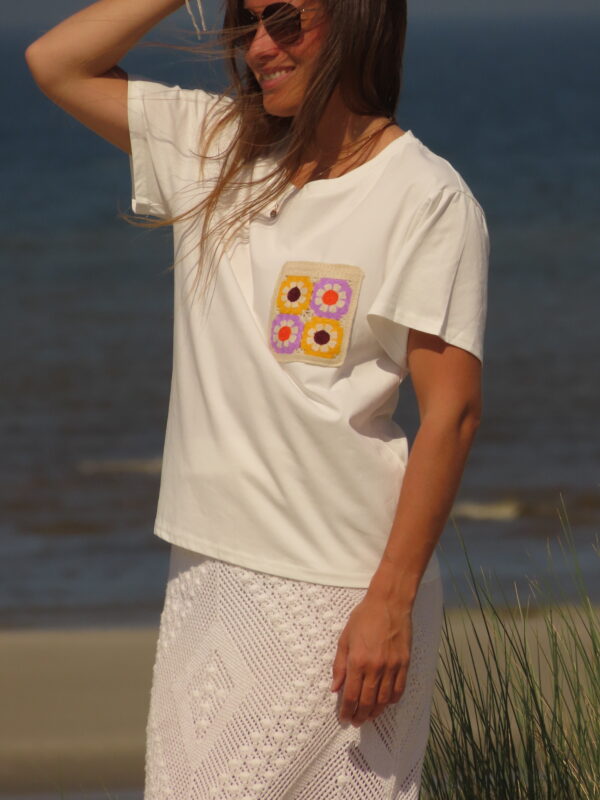 Tee-shirt blanc à manches courtes avec poche décorative florale en macramé sur le côté cœur.