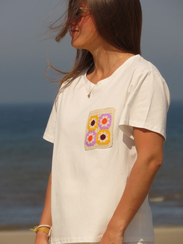 Tee-shirt blanc à manches courtes avec poche décorative florale en macramé sur le côté cœur.