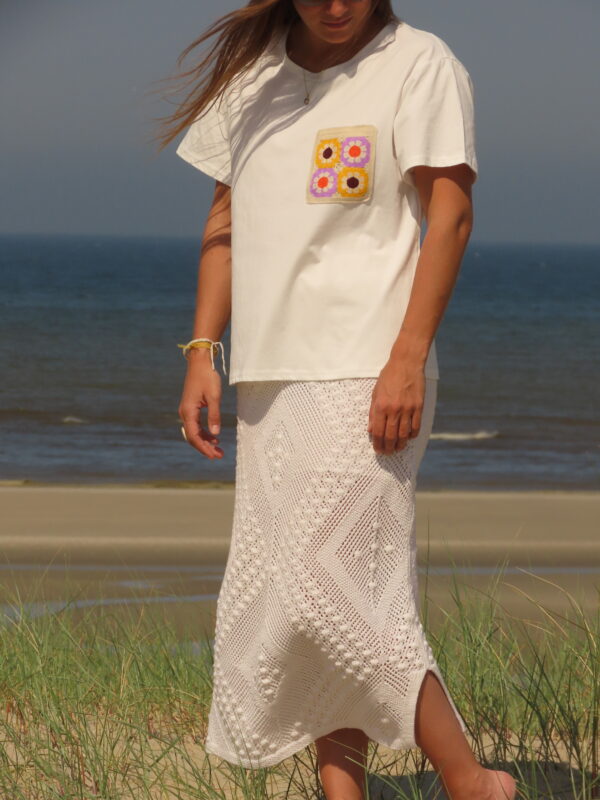 Tee-shirt blanc à manches courtes avec poche décorative florale en macramé sur le côté cœur.