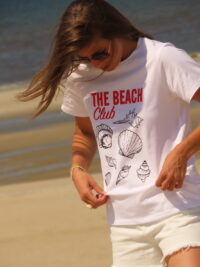 Tee-shirt blanc 100% coton, manches courtes, imprimé "Beach Club" en rouge avec motifs de coquillages noirs.