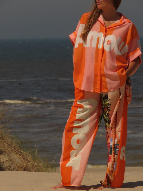 Pantalon Amour ample avec élastique à la taille, imprimé "Amour" sur une jambe et motif bord de mer sur l'autre, rayures roses et oranges