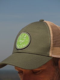 Homme portant une casquette trucker kaki Sea View sur une plage de sable, face à l'océan