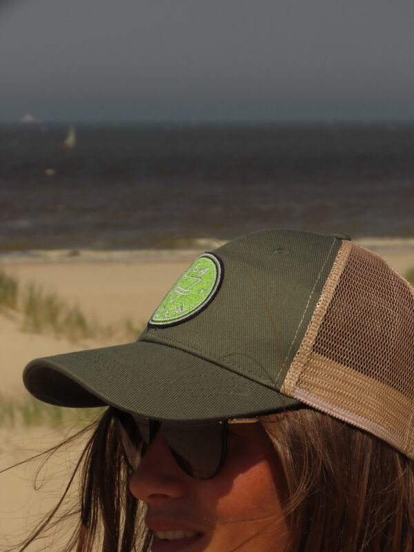 Femme portant une casquette trucker kaki Sea View sur une plage de sable, face à l'océan