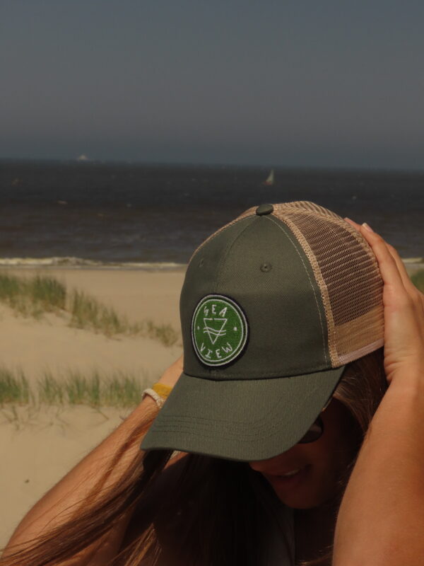 Femme portant une casquette trucker kaki Sea View sur une plage de sable, face à l'océan