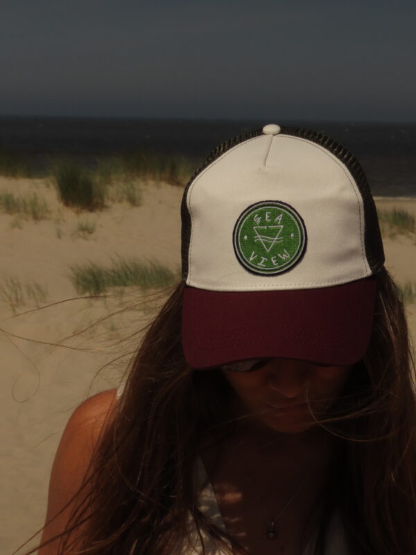 Casquette trucker blanche avec visière kaki et filet bordeaux, ornée d'un écusson Sea View brodé sur le devant.